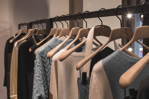 Παλτό και πουλόβερ ανοιχτό καφέ και γκρι χρώματα στην κρεμάστρα στο κατάστημα. Κλασικά γυναικεία ρούχα μόδας. - Φωτογραφία, εικόνα
