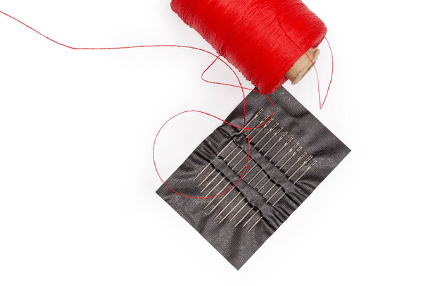 Handnähnadeln unterschiedlicher Länge mit Ösen mit einfacher Fadenöffnung oben in einem Kunststoffhalter und Spule aus roten Fäden, Fragment Nahaufnahme, Ansicht von oben - Foto, Bild