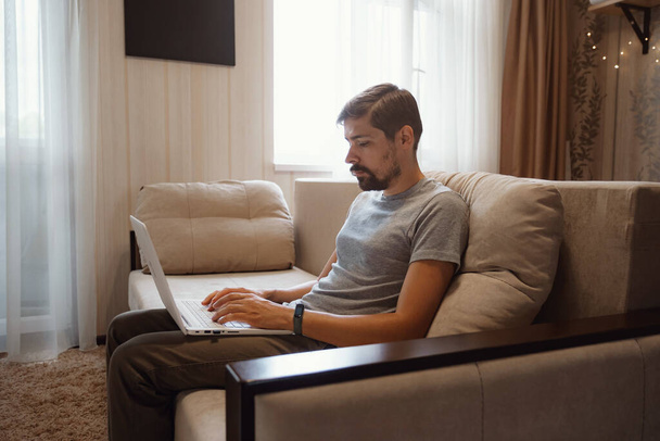 Pensive γενειοφόρος άνθρωπος κάθεται σε καναπέ εργασίας στο φορητό υπολογιστή σκέψης της λύσης πρόβλημα, στοχαστικός αρσενικό εργαζόμενο μελετώντας την ιδέα κοιτάζοντας οθόνη υπολογιστή λήψη απόφασης - Φωτογραφία, εικόνα