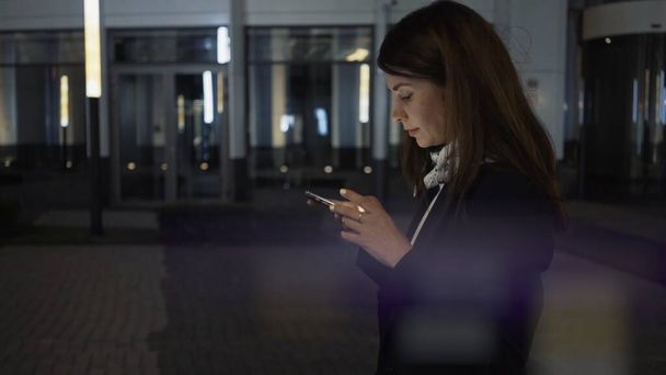 Woman profile shot walking with a phone wearing a black jacket, night shot  - Foto, immagini