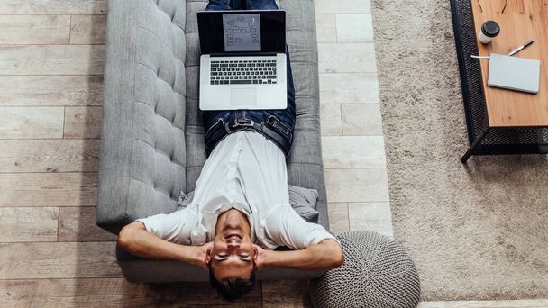 happy man with a laptop lying on the couch . - Фото, изображение