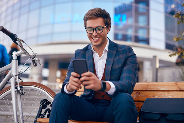 Happy formal guy with bike text messaging on smartphone - Zdjęcie, obraz