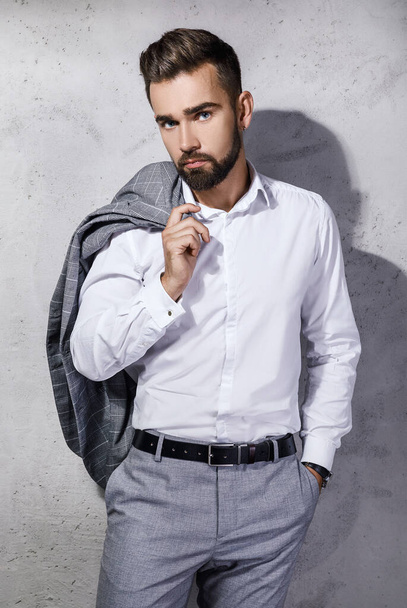 Handsome bearded man wearing gray suit is posing against concrete wall - 写真・画像