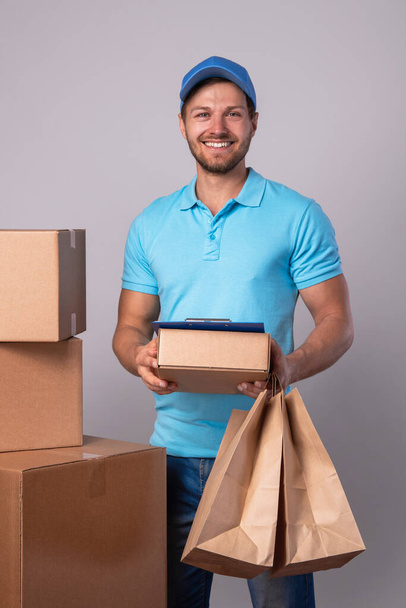 Happy delivery man during work with a packages in a cardboard boxes over gray background - Fotoğraf, Görsel