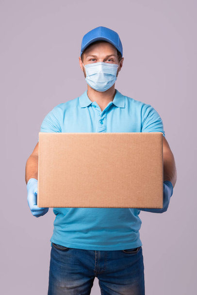 Young delivery man is wearing prevention mask and gloves with a cardboard boxes isolated on gray background - Фото, зображення