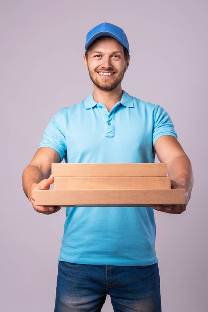 Fiatal futár dobozokat tart egy finom pizzával elszigetelve a szürke backgrounon. - Fotó, kép