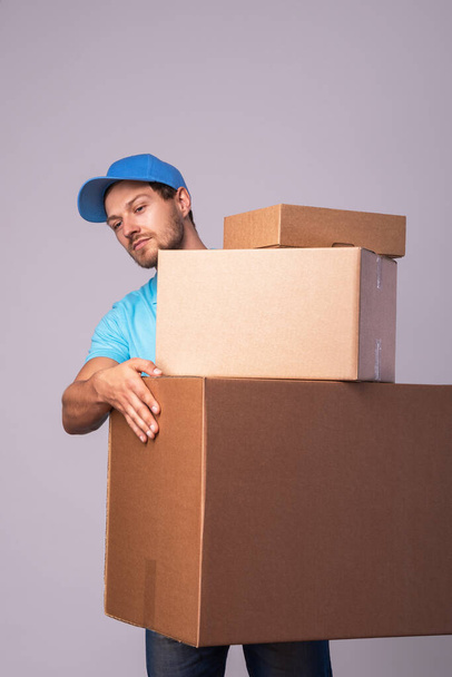 Happy delivery man tijdens het werk met een pakje in een kartonnen doos over grijze achtergrond - Foto, afbeelding
