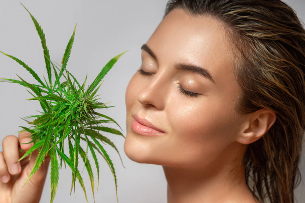 Conceito de cosméticos CBD. Mulher bonita com uma folha de cannabis no fundo cinza - Foto, Imagem