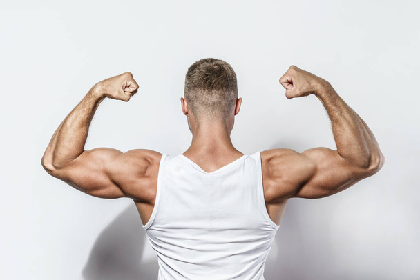 Young bodybuilder man showing his muscular arms against gray background - 写真・画像