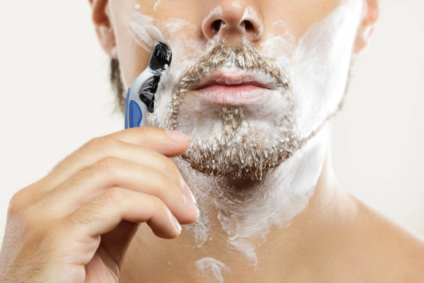 Jeune homme avec un rasoir de sécurité et de la crème à raser sur le visage - Photo, image