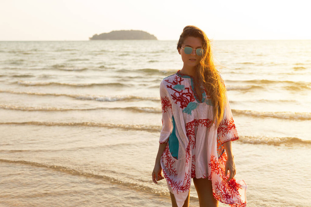 Joven mujer encantadora con hermoso vestido está caminando por la orilla del mar durante la puesta del sol - Foto, imagen
