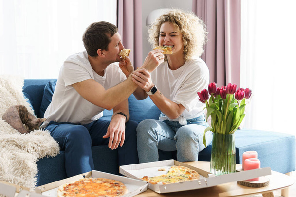 Young and happy couple eating delicious pizza at home - Фото, изображение