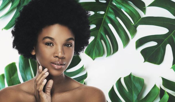 Jonge en mooie Afrikaanse vrouw met een perfecte gladde huid in tropische bladeren. Begrip natuurlijke cosmetica en huidverzorging. - Foto, afbeelding