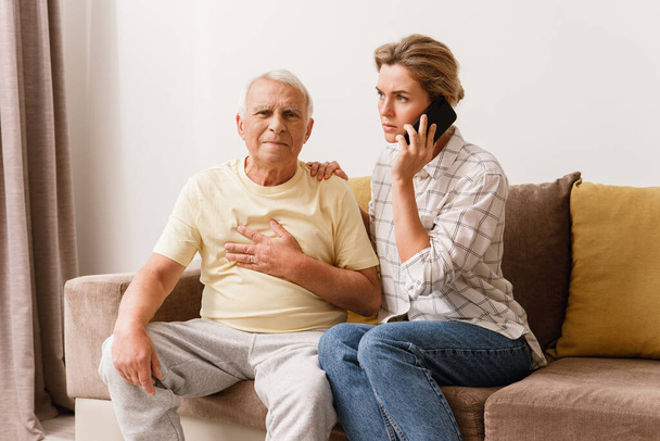 Anxious woman  calling to 911 emergency line because her elderly father with a coronary disease having heart attack symptoms at home - Foto, Imagem