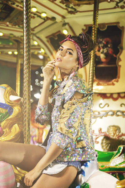 Stylish woman wearing sparkling jacket on the carousel in theme park - Fotografie, Obrázek