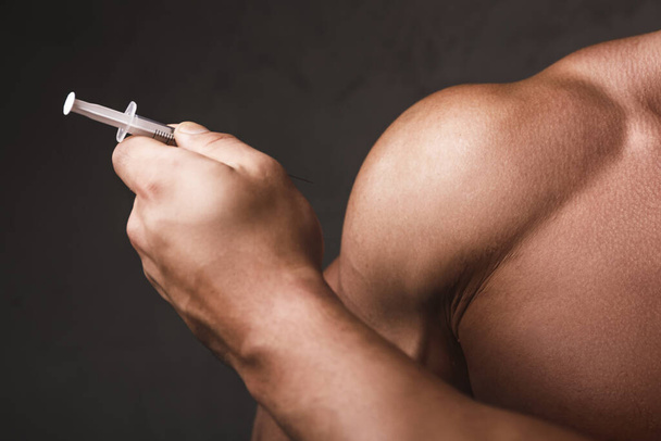 Muscular man with a syringe in his hand. Concept of a strength workout and anabolic steroids usage. - Fotoğraf, Görsel