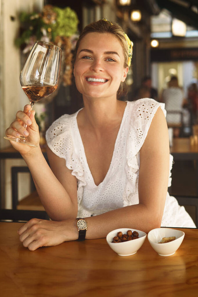Portrait of beautiful and joyful woman with a glass of wine in a city cafe - 写真・画像