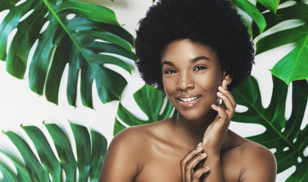 Genç ve güzel bir Afrikalı kadın. Tropikal yaprakların içinde pürüzsüz bir teni var. Doğal kozmetik ve cilt bakımı kavramı. - Fotoğraf, Görsel