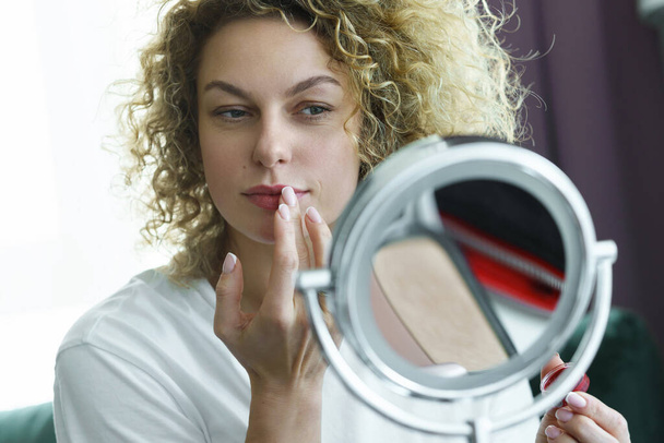 Young and beautiful woman looking into a mirror and applying lip balm - Foto, Imagen