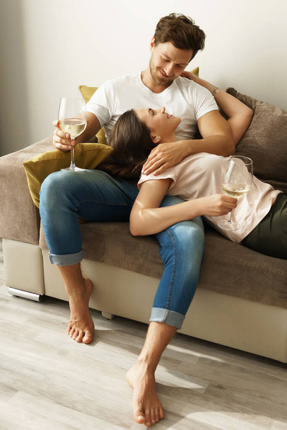 Young and happy couple drinking wine and relaxing at home - Photo, Image