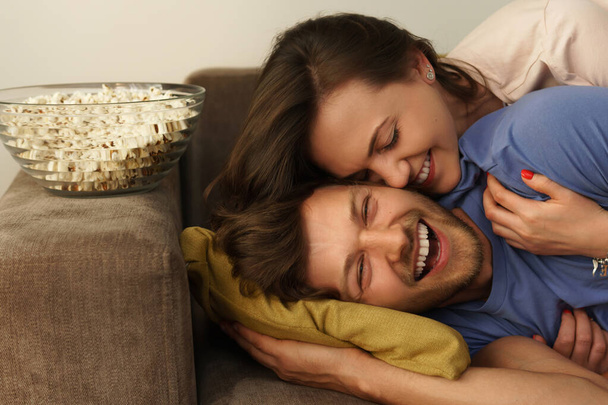 Young and happy couple watching comedy TV show at home - Фото, изображение