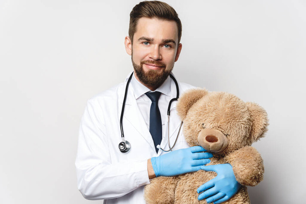 Professional pediatrician with a teddy bear in his hands on gray background - Foto, immagini