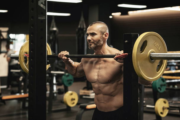 Handsome bearded bodybuilder during his workout with a barbell in the gym - Photo, Image