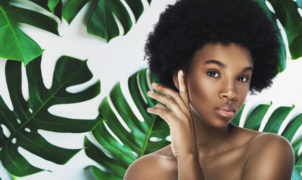 Mujer africana joven y hermosa con perfecta piel lisa en hojas tropicales. Concepto de cosmética natural y cuidado de la piel. - Foto, Imagen