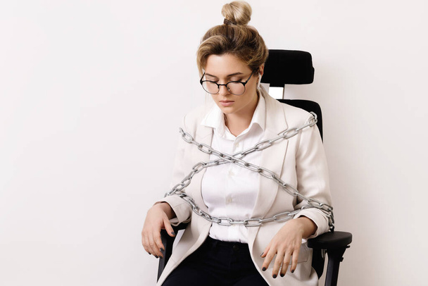 Upset business woman tied up to the office chair with a chains. Concept of debts or overtime work. - Photo, Image