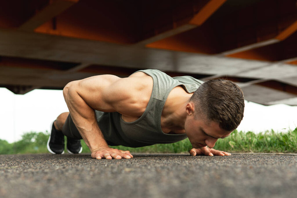 Homem jovem e musculoso está fazendo flexões durante o treino calistênico em uma rua - Foto, Imagem