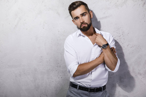 Portrait of handsome  bearded man wearing white shirt is posing against concrete wall - Foto, afbeelding