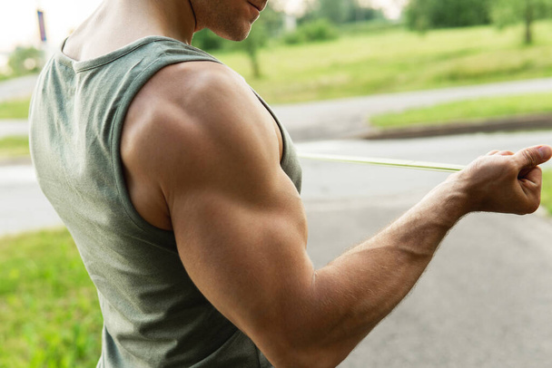 Muscular man during  workout with a resistance rubber bands outdoors. - Photo, image