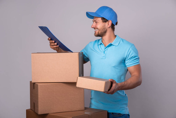 Happy delivery man during work with a packages in a cardboard boxes over gray background - Foto, imagen