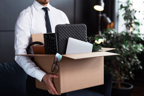 Молодого человека увольняют с работы. Бизнесмен и картонная коробка со своими личными вещами с работы. - Фото, изображение