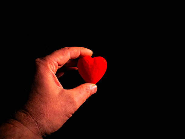 Coeur symbole de la Saint-Valentin à la main sur fond noir. Symbole coeur rouge. Saint Valentin. Palmes de mains masculines. Un sentiment d'amour. Fond noir. La relation entre un homme et une femme. - Photo, image