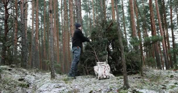 obóz przetrwania dziczy - człowiek budujący domek na gałęzi drzewa w lesie zimą - Materiał filmowy, wideo