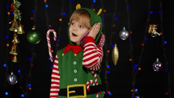 Niña en Navidad elfo Santa Claus ayudante traje haciendo felicitaciones llamada en el teléfono móvil - Imágenes, Vídeo