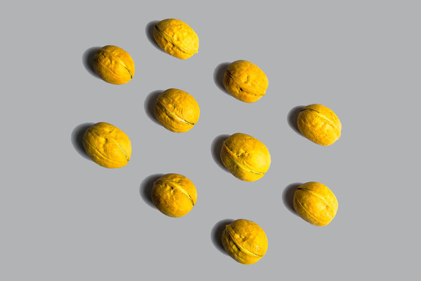 Gele walnoten in schelpen liggen in rijen op pastelgrijze rug. Creatieve food mockup in trendy kleuren 2021. Bovenaanzicht. Hoge kwaliteit foto - Foto, afbeelding