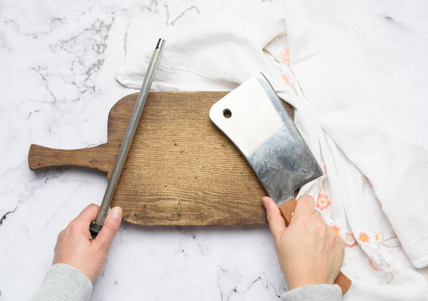 vrouwelijke handen houden een keukenmes en een slijper met een handvat, het proces van het slijpen van gebruiksvoorwerpen, bovenaanzicht - Foto, afbeelding