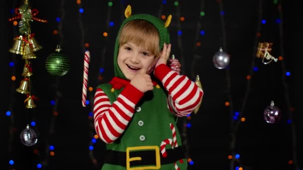 Niña en Navidad elfo Santa Claus ayudante traje haciendo felicitaciones llamada en el teléfono móvil - Imágenes, Vídeo