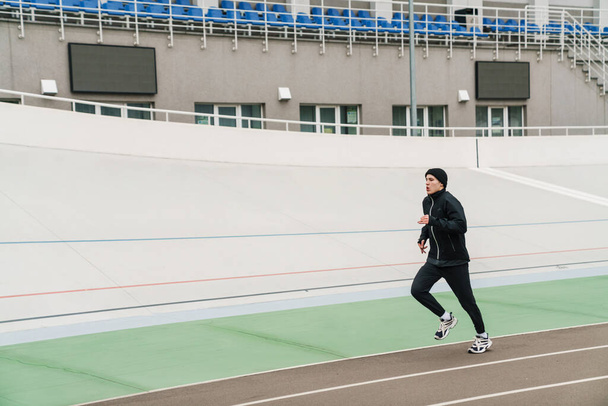 Handsome athletic sportsman running while working out at stadium outdoors - Foto, afbeelding