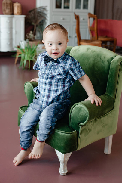 A little boy with  Down Syndrome is sitting in a green chair in the studio. The concept of care for the disabled. Family story. Mothers Day. Coppy Space. Toning. - Foto, immagini