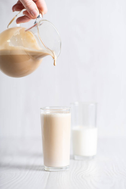 Dalgon brown coffee mixture is poured from the decanter into a glass of milk. Milkshake with instant coffee and sugar, whipped until thick foam. - Foto, imagen