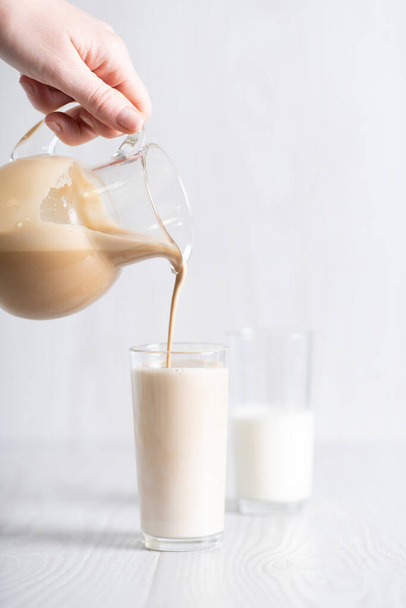 Dalgon brown coffee mixture is poured from the decanter into a glass of milk. Milkshake with instant coffee and sugar, whipped until thick foam. - Φωτογραφία, εικόνα