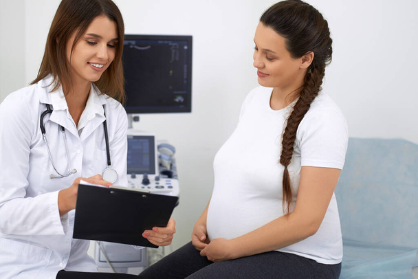 Pregnant lady talking with doctor during regular examination - Foto, Bild