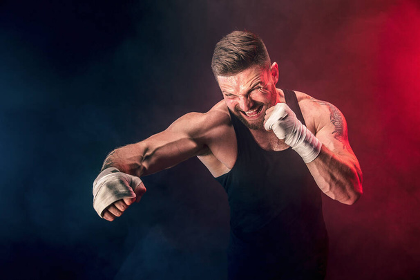 Sportsman muay thai boxer fighting on black background with smoke. Sport concept - Фото, изображение