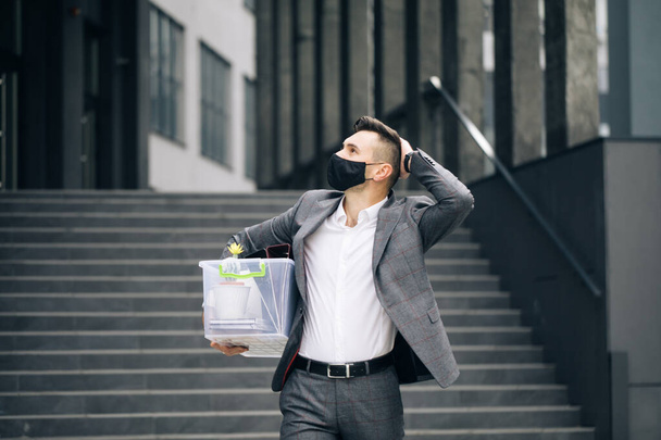 Sad male office worker in depression with box of personal stuff. Businessman lost job. Fired man walking outdoor. Depressed jobless person. Unemployment concept. Left without money. - Photo, image