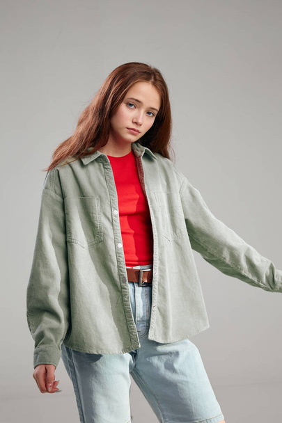 beautiful girl in red t-shirt jeans and jacket on gray background cropped view - 写真・画像