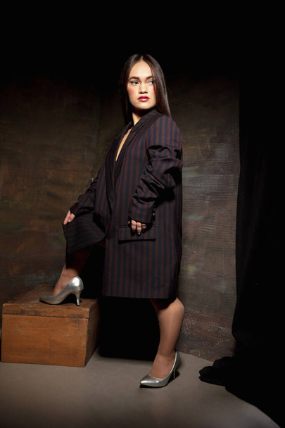 Caucasian female inclusive model posing on dark studio background in classic black outfit - Фото, изображение