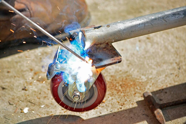 Worker with a welding machine fixing a caster wheels with fiery sparks flying around - Foto, Imagem